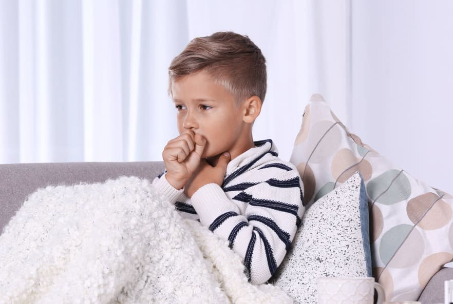 Ill boy suffering from cough on sofa at home