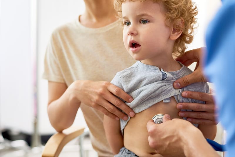 Child Visiting Doctor with Mom A child being held by his mom as the doctor checks his heart rate