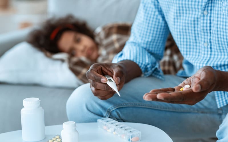 A sick, young girl in bed while her dad takes care of her and gets her medication ready