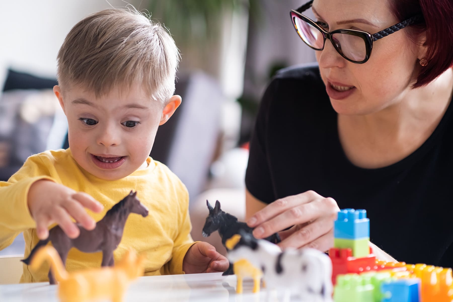 parent-bonding-with-their-child-with-down-syndrome-2024-12-04-16-57-57-utc Young child with Down syndrome excitedly playing with animal toys while bonding with a caregiver, highlighting joyful interaction and developmental support.