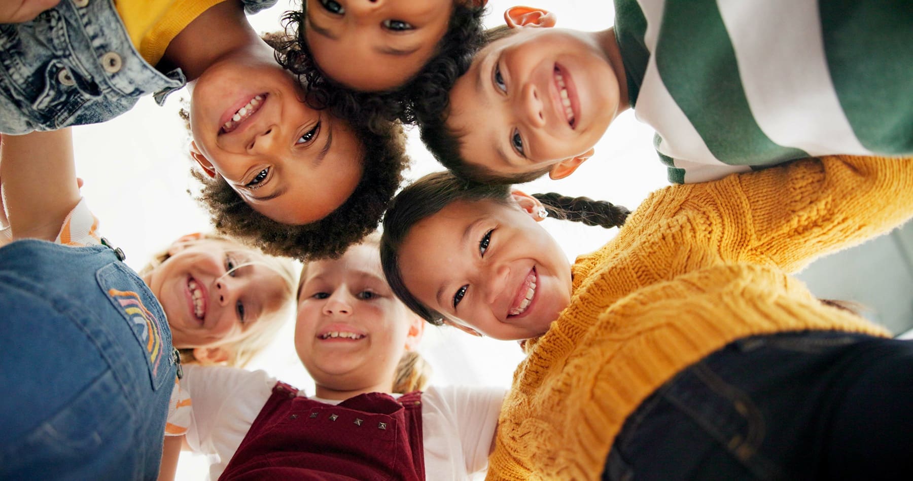 Diverse group of smiling children huddled together in a circle, symbolizing emotional support, friendship, and resilience in a positive school environment.