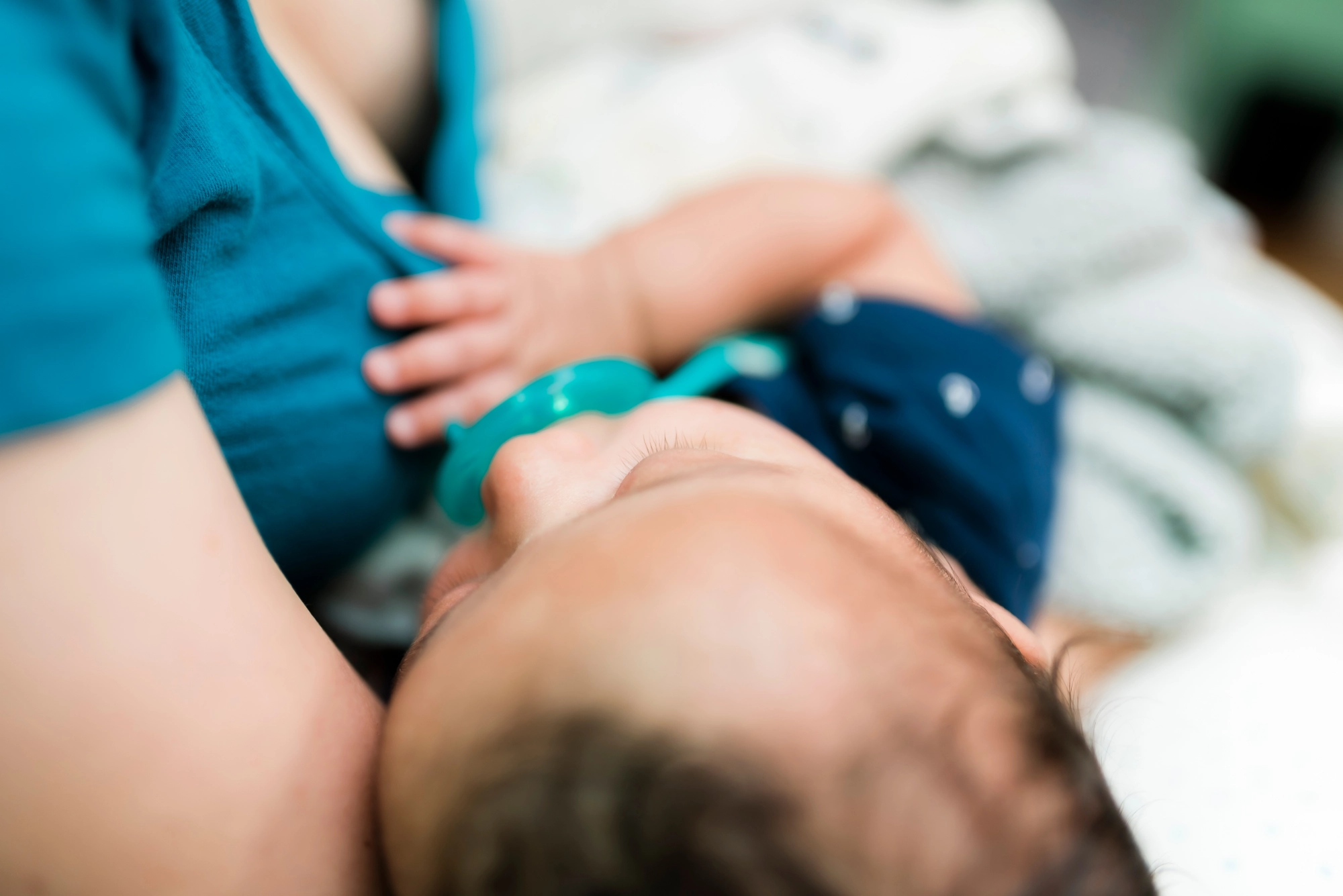 Close-up of a baby breastfeeding while being held, focusing on the infant’s face and caregiver’s chest.